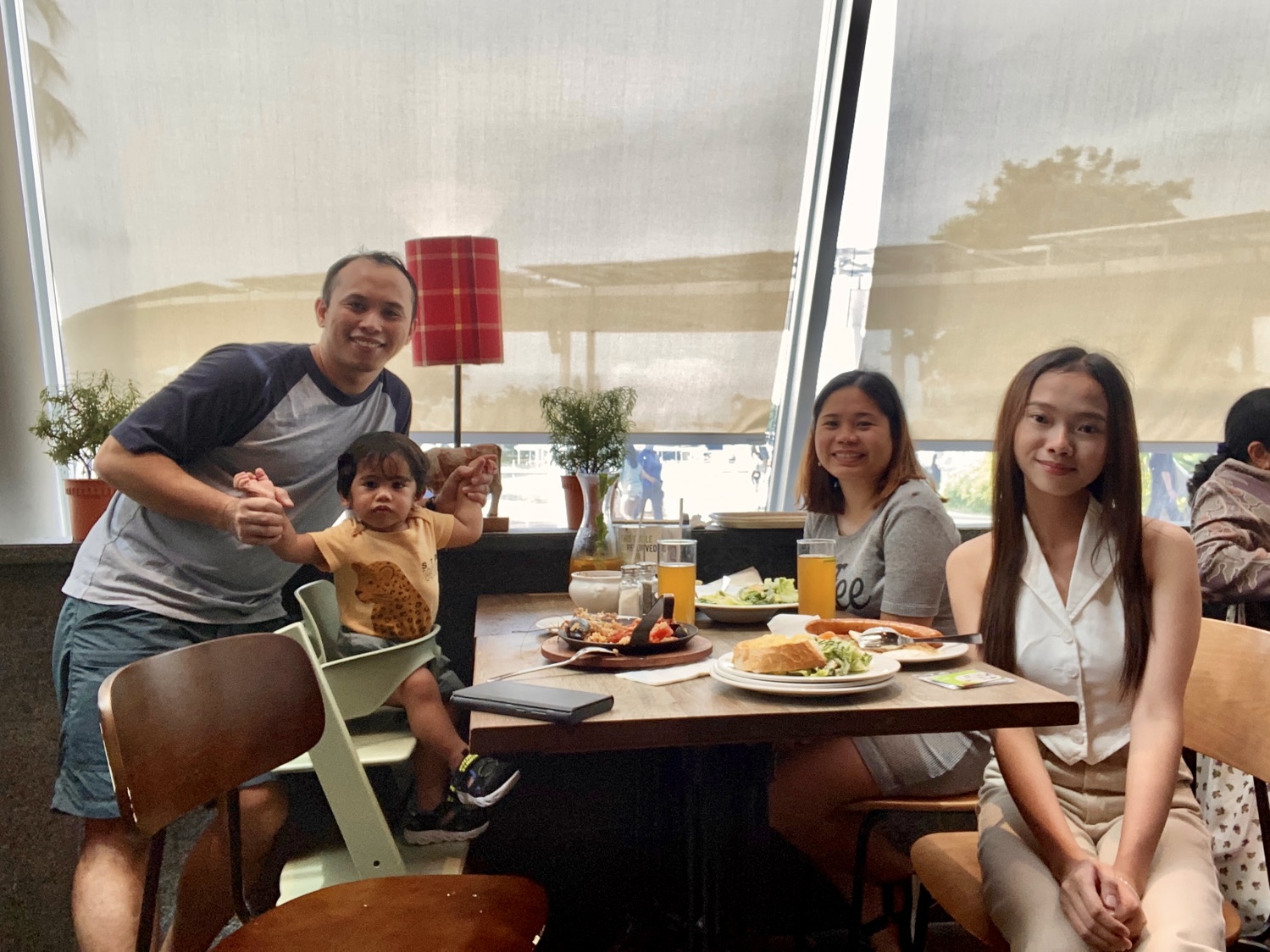 Three adults surround a dining table to have lunch. A baby also sits on a high chair.
