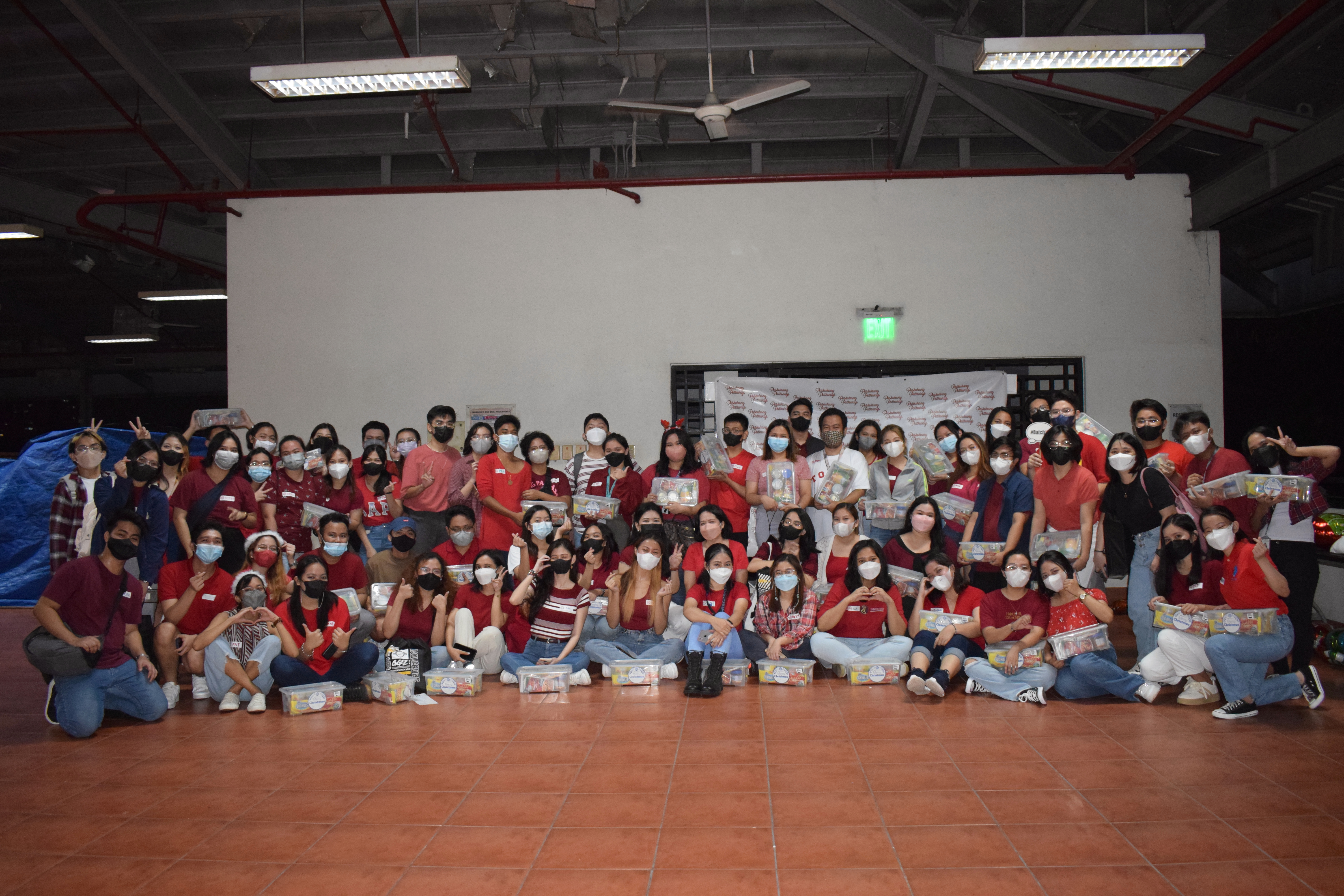 Two rows of college students in red pose for a group photo showcasing their Noche Buena packages.