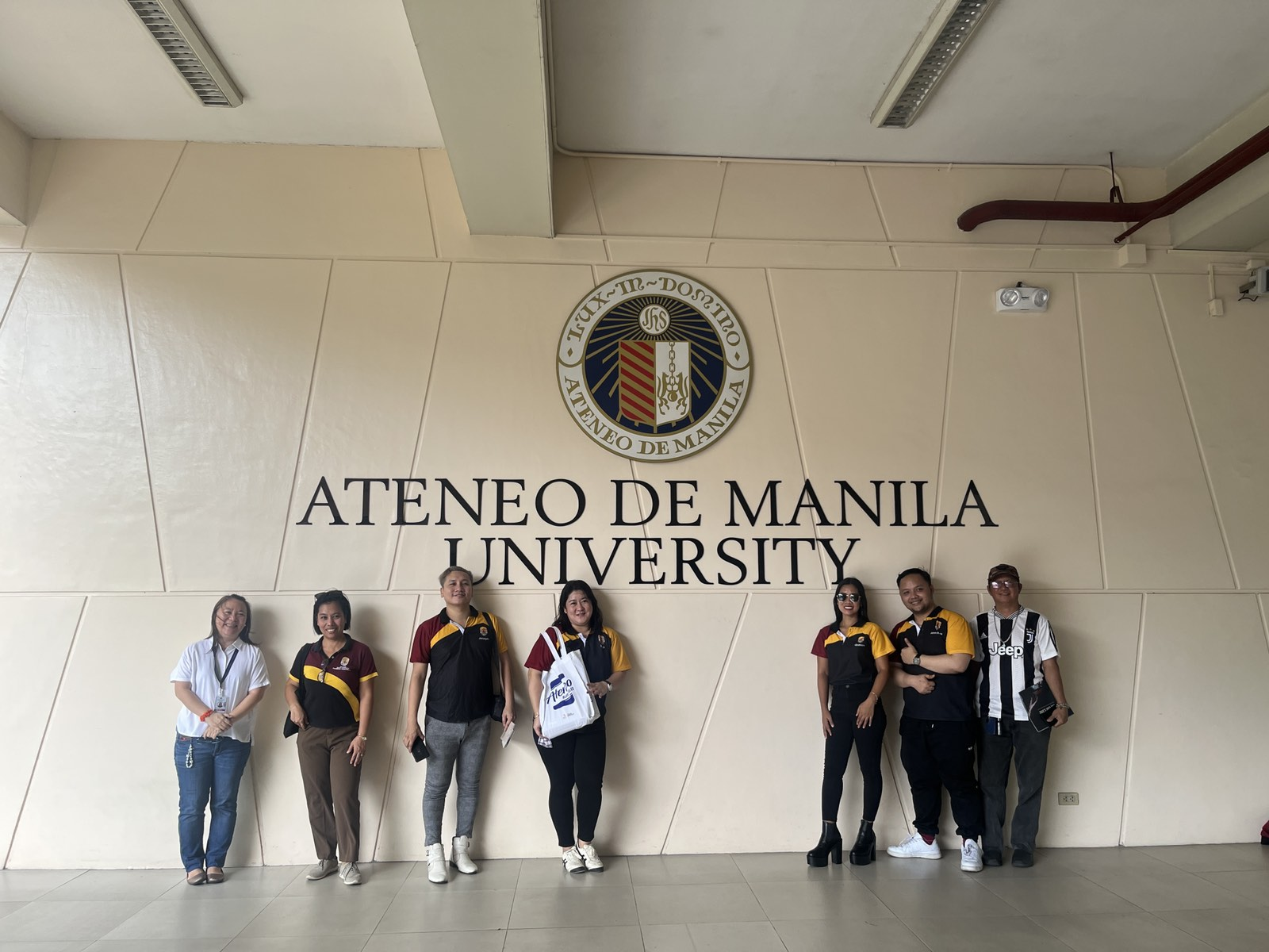 The Office of University Development & Alumni Affairs (OUDAA) and University of Perpetual Help System DALTA – Molino Campus (UPHSDM) team pose in front of Ateneo de Manila University's official seal.